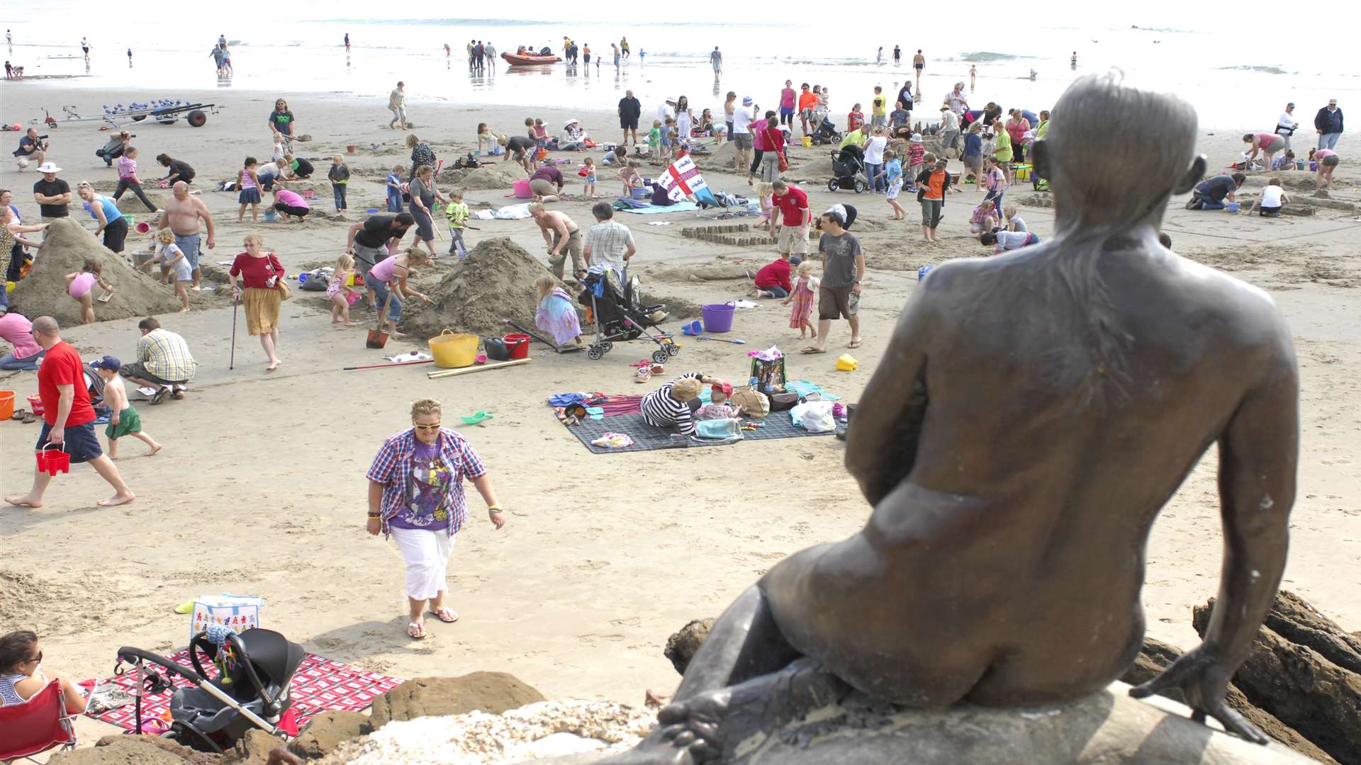 A busy Sunny Sands beach in Folkestone overlooked by Cornelia Parker's permanent Triennial exhibit the Folkestone Mermaid
