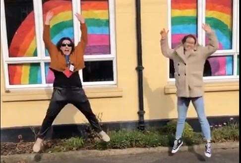 Year 2 teachers Sam Mulock and Cerys Finch jumping for joy next to a large rainbow created by staff and pupils