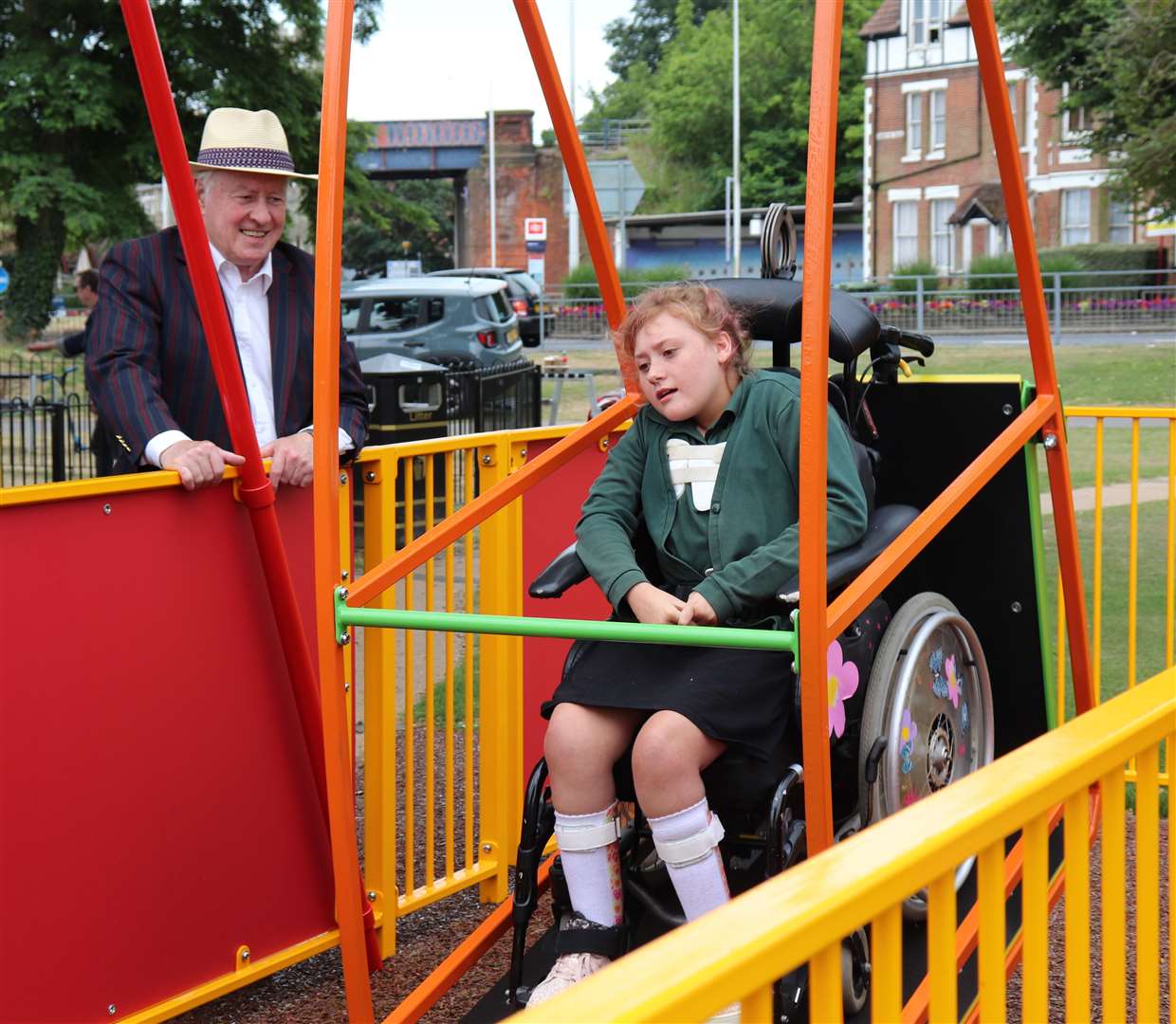 Lucy from Beacon Park School tries out the new wheelchair swing in Radnor Park, Folkestone, watched by council leader Cllr David Monk