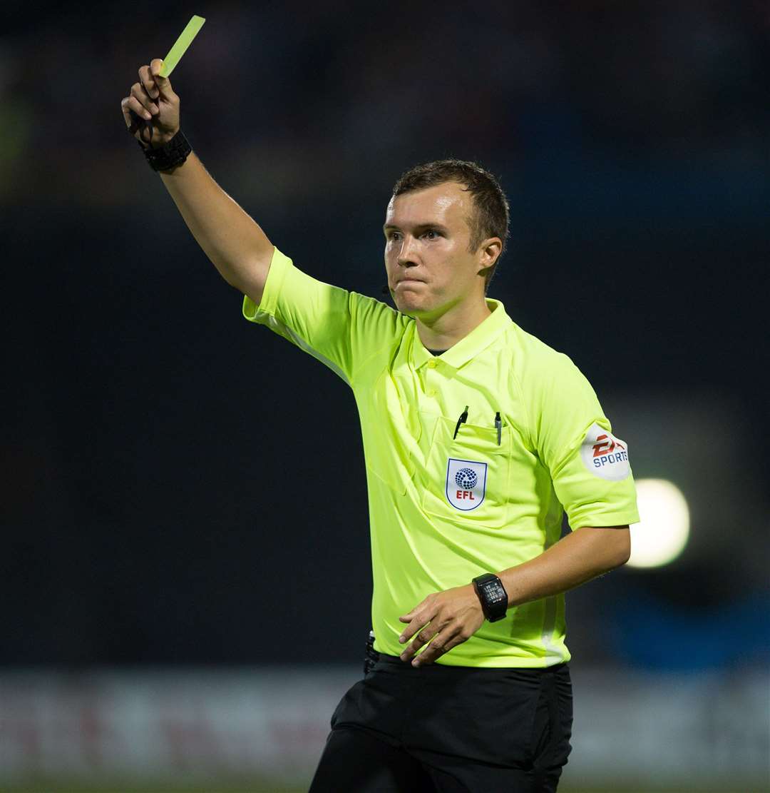 Referee Antony Coggins brandishes a yellow card during a Gillingham match