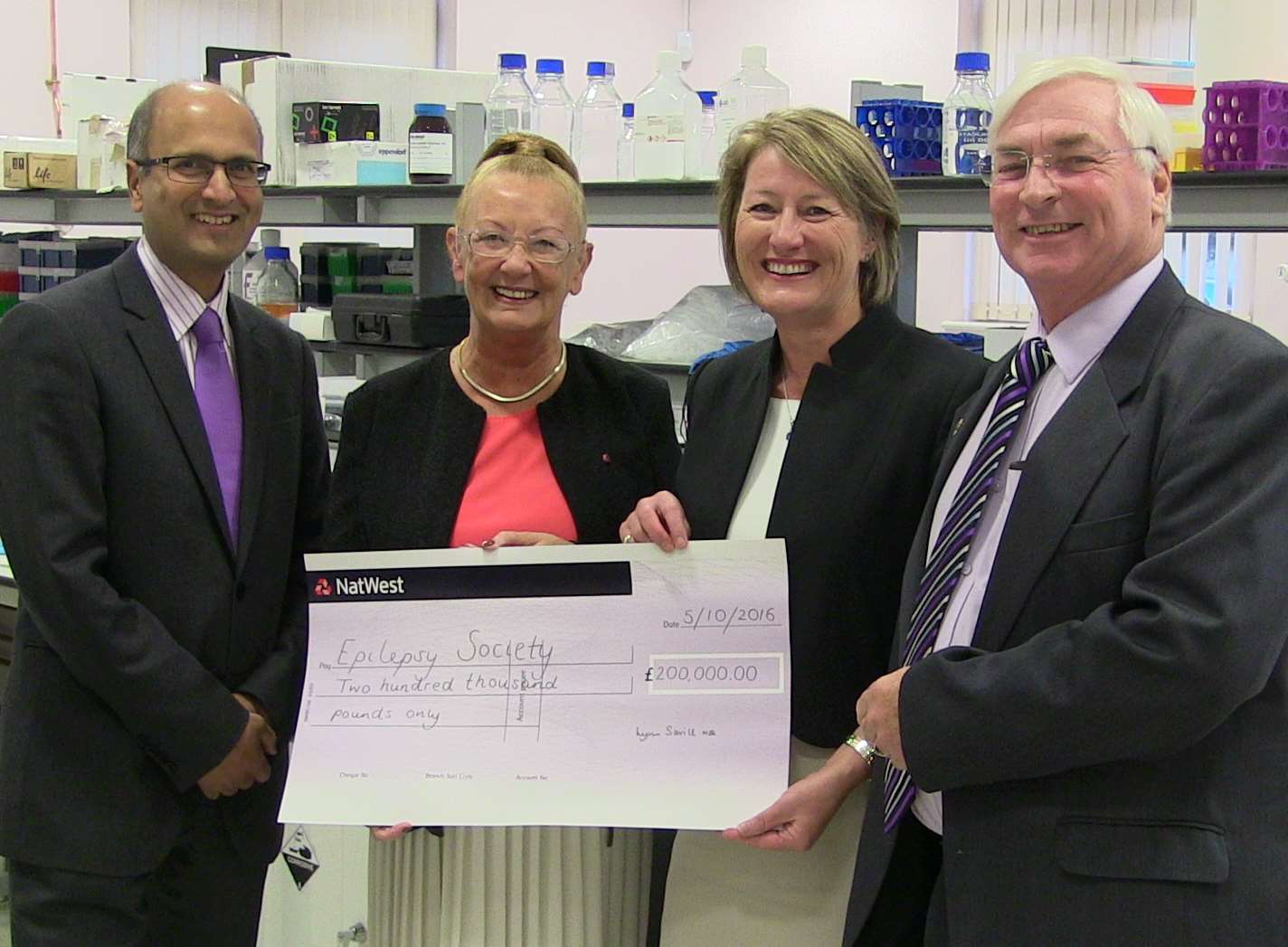 Fred and Lynn Savill present a cheque for £200,000 to Epilepsy Society at the charity's research centre in Buckinghamshire. From left to right: Professor Sanjay Sisodiya, director of genomics at Epilepsy Society; Lynn Savill; Rosemarie Finley, chief executive at the charity; and Fred Savill.
