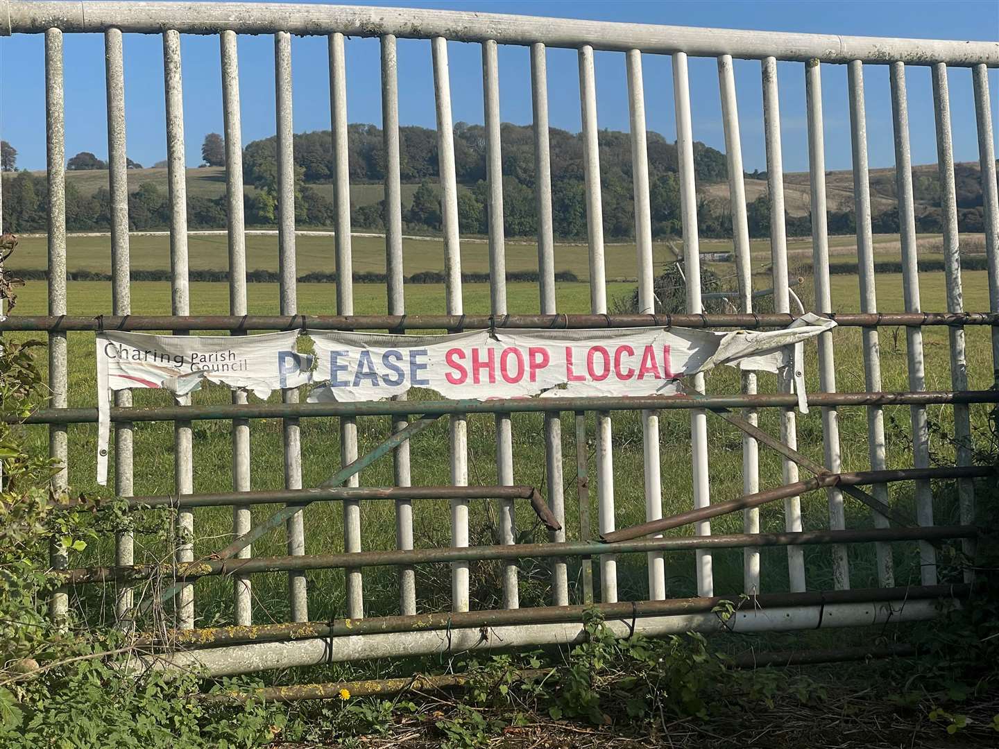 A battered Charing Parish Council sign supporting 'shop local' campaigns lies opposite where the new supermarket will go
