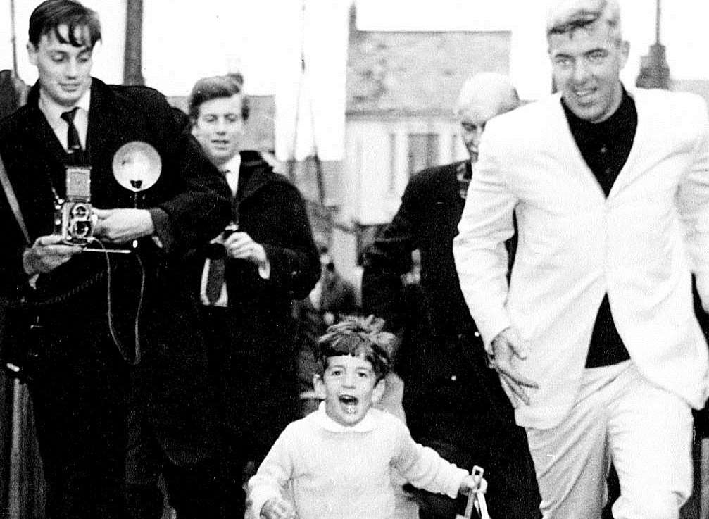 John F Kennedy Jnr races for the beach accompanied by his bodyguard and a clutch of Fleet Street photographers