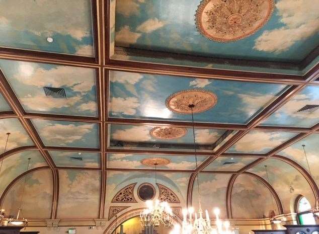 Up above the chandeliers the high ceiling features a blue sky and fluffy white clouds
