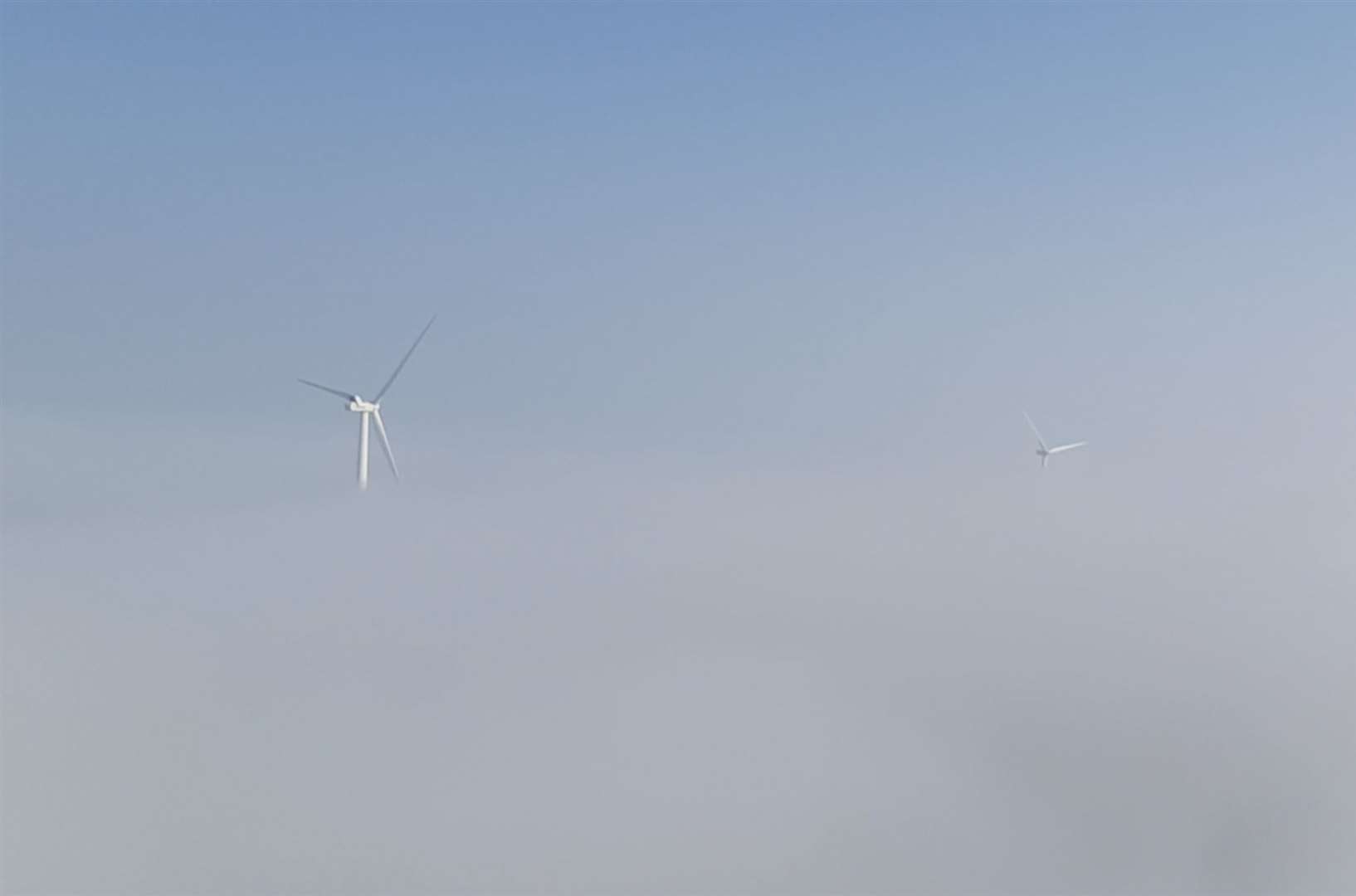 On a foggy day the technicians can only see the tops of the turbines.