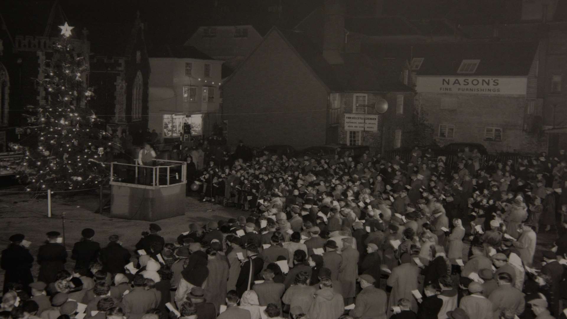 A Christmas scene from Canterbury in 1955 - carol singing around the Christmas tree in the Marlowe Theatre car park on Christmas Eve, when the Archbishop, Dr Geoffrey Fisher, gave the blessing.