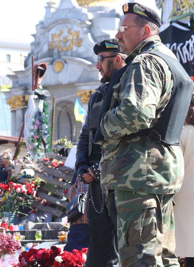 Members of a self-defence unit standing in front of floral tributes to the dead in Kiev