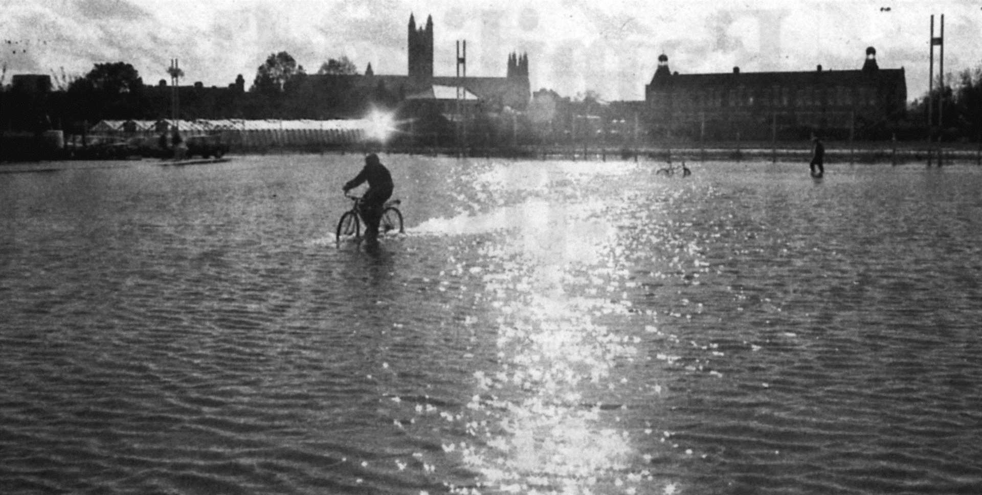 Canterbury Cathedral provides the backdrop as a cyclist rides through flood water