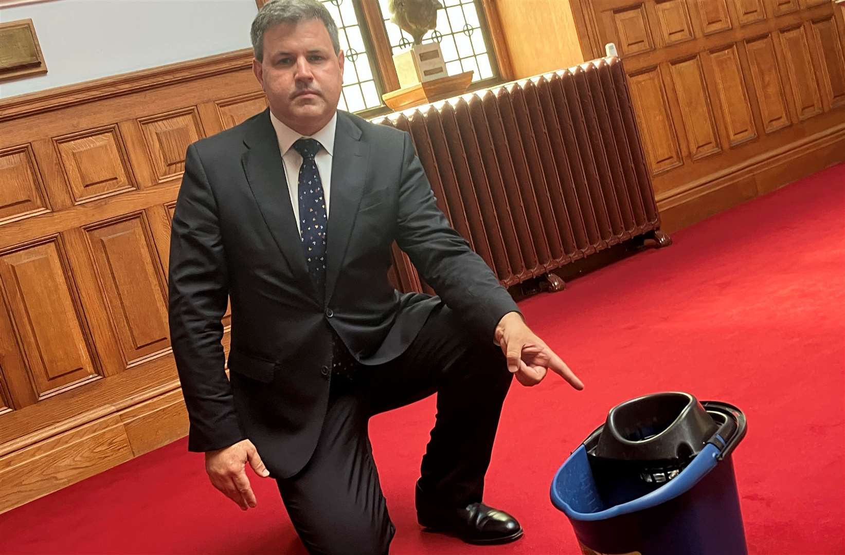 Lib Dem leader Cllr Antony Hook pointing to a bucket collecting water from the leaking roof at County Hall in Maidstone