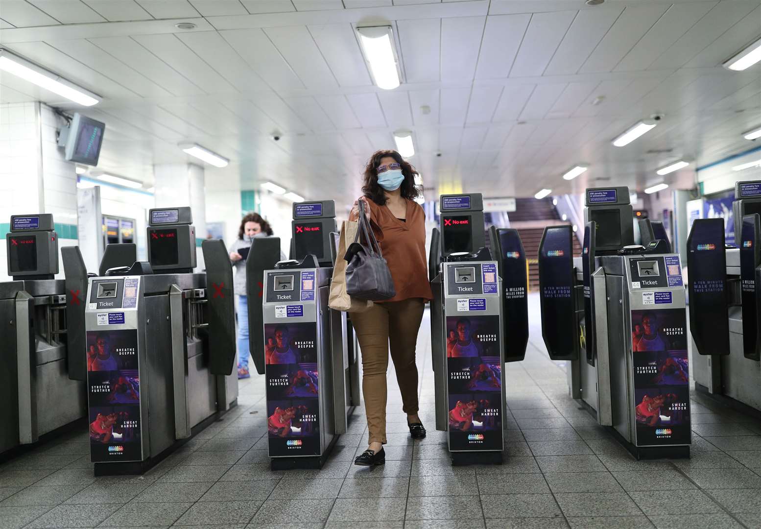 A woman wears a face mask as she exits the ticket barriers at Brixton Underground station in south London (Yui Mok/PA)