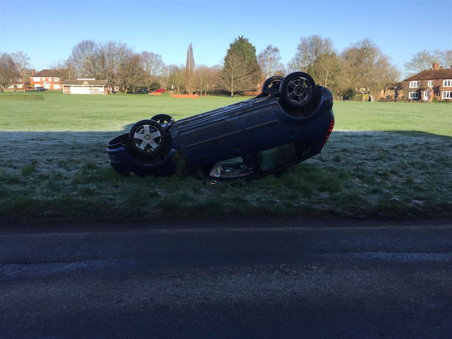 The blue ford is lying upside down on the cricket green