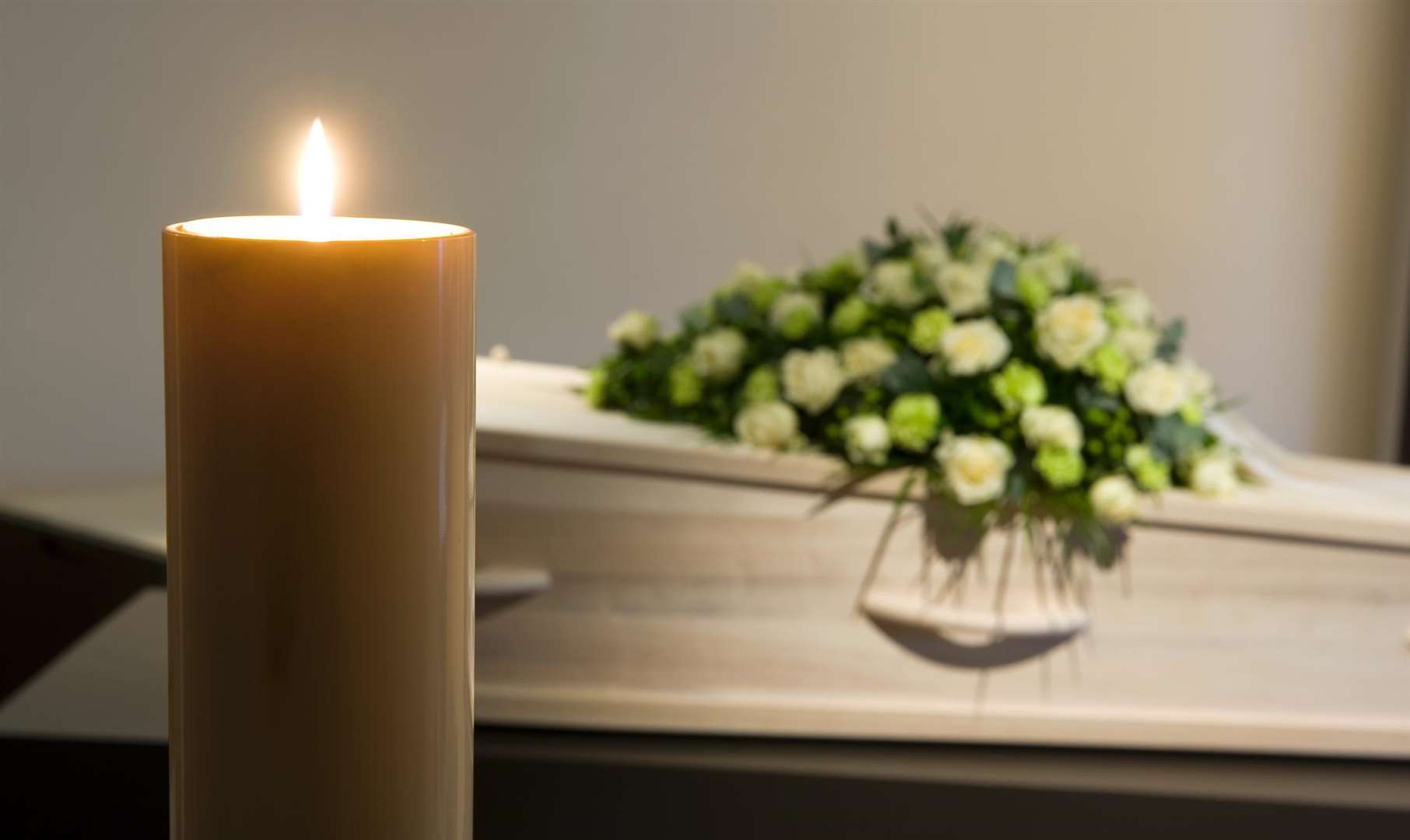 A burning candle with a coffin and a flower arrangement on the background in a mortuary. Stock picture