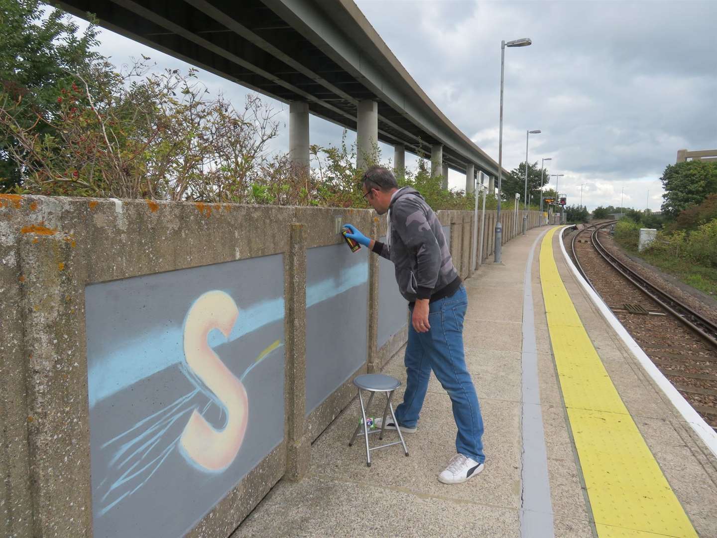 Artist Graham Upton at work on Swale Halt's platform mural. Picture: Kent Community Rail Partnership