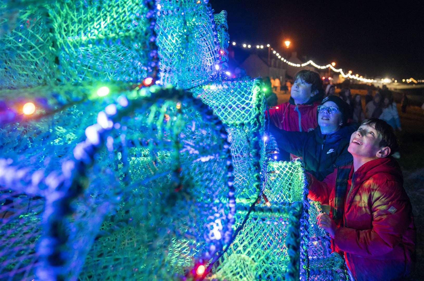 Luca Mowbrary, 12; Dan MacRae, 11; and Daniel Mason, also 11, take a closer look at the lights on the Christmas tree made of fishing creels on the harbour-side in the Scottish village of Ullapool (Jane Barlow/PA)
