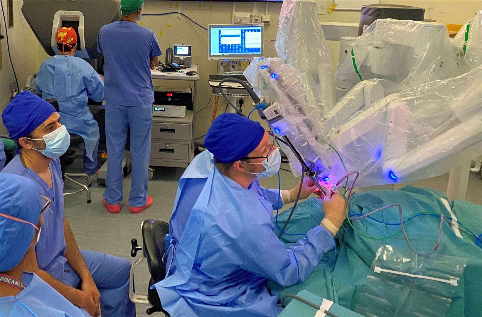 The head and neck team using the robot at Kent and Canterbury. In the photo, the surgeon is top left, with his back to the camera and looking into the console, while the robot is attached to the patient on the table. Picture: NHS