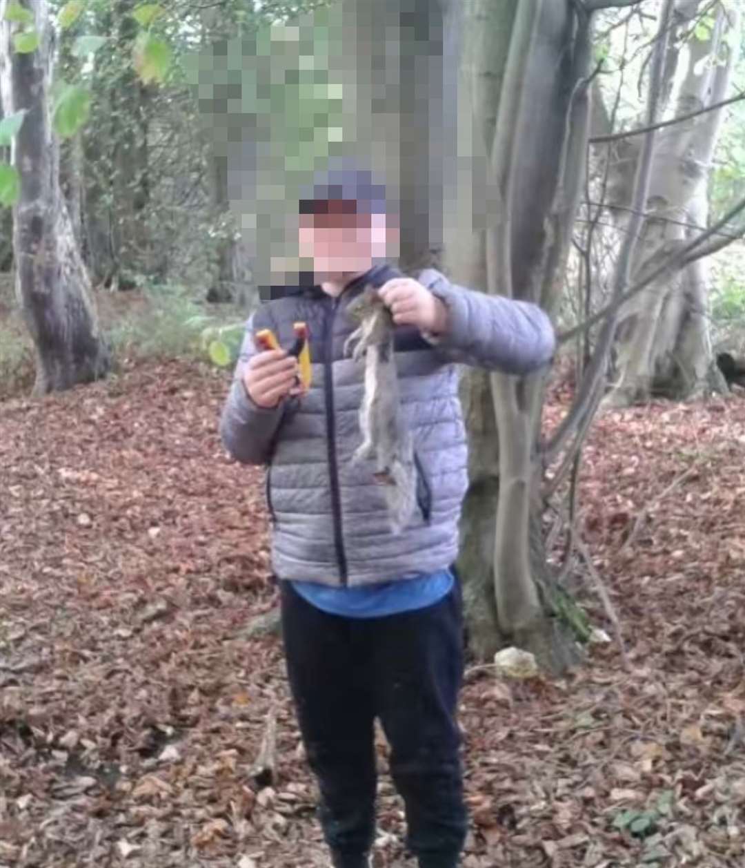 A young boy holding a catapult in one hand and a dead squirrel in the other, shared on TikTok