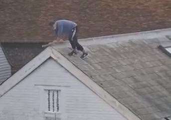 The man holds on to the roof as he moves perilously close to the edge