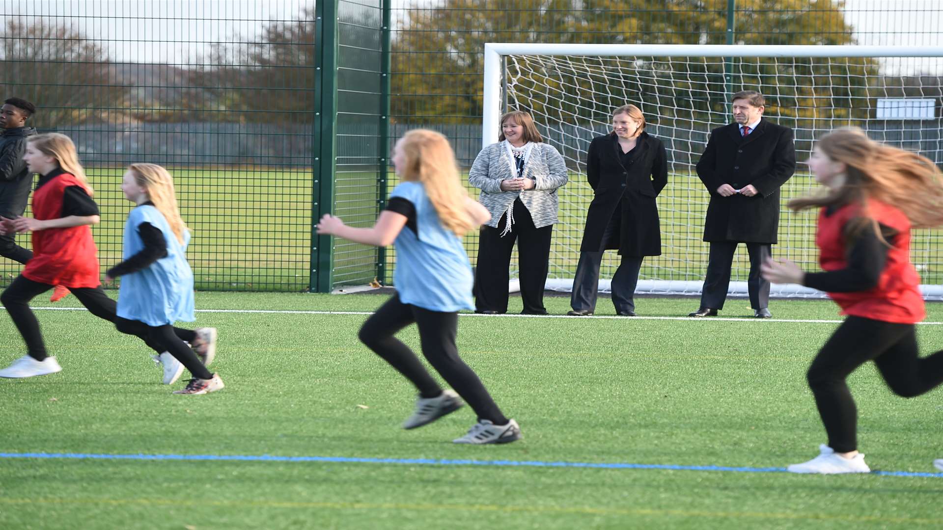 Victory Academy principal Mandy Gage, sports minister and Chatham MP Tracey Crouch and the Football Foundation's chief executive officer, Paul Thorogood, watch students using the new pitch