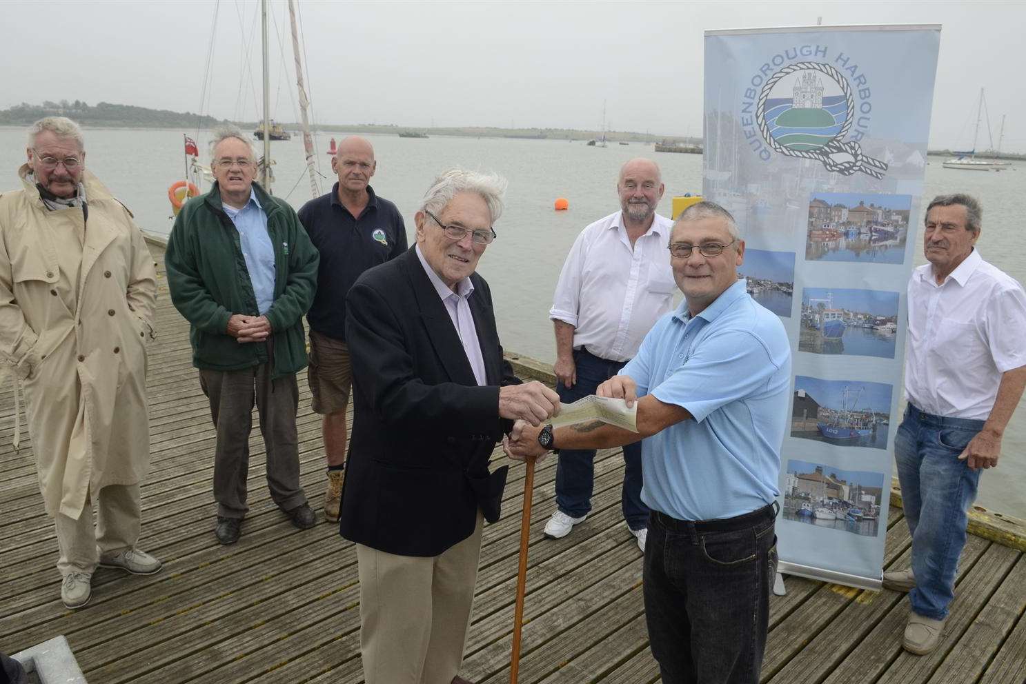 Bob Eatwell, chairman of the Queenborough Harbour Trust, watched by fellow members, presents Eddie Johnson with a cheque for £500.
