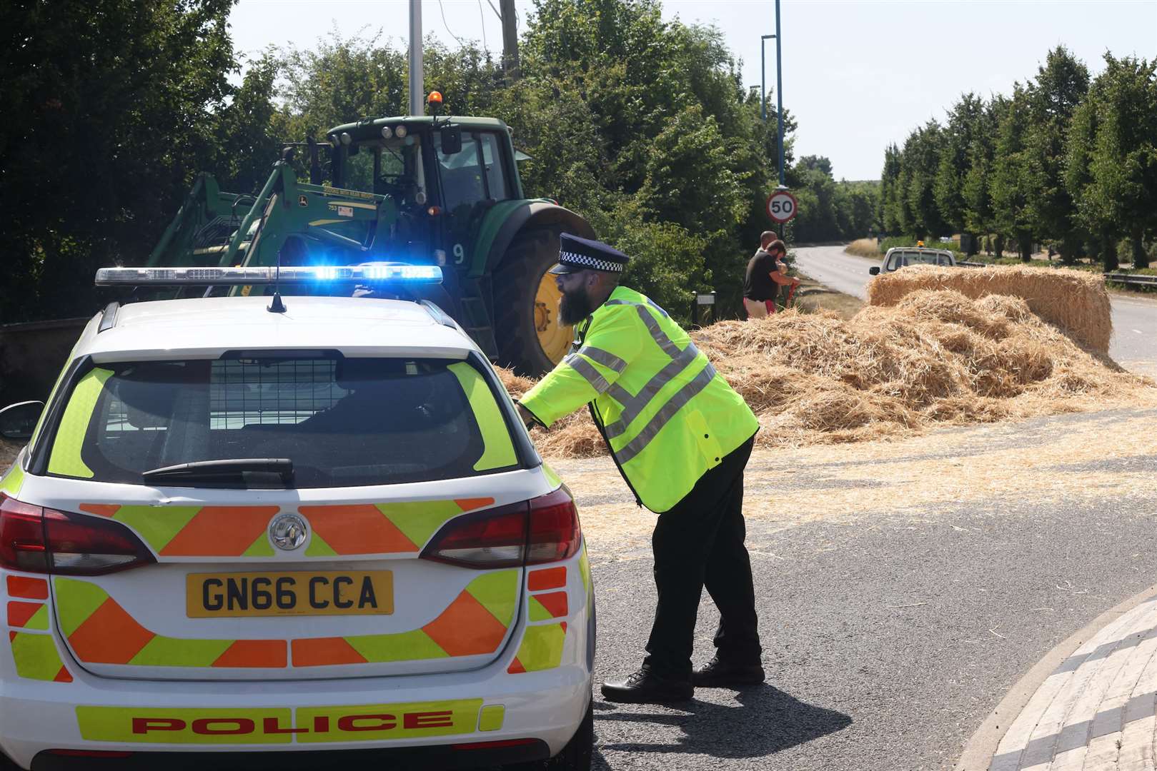 Police closed the road while two men worked to clear the fallen hay. Images: UKNIP