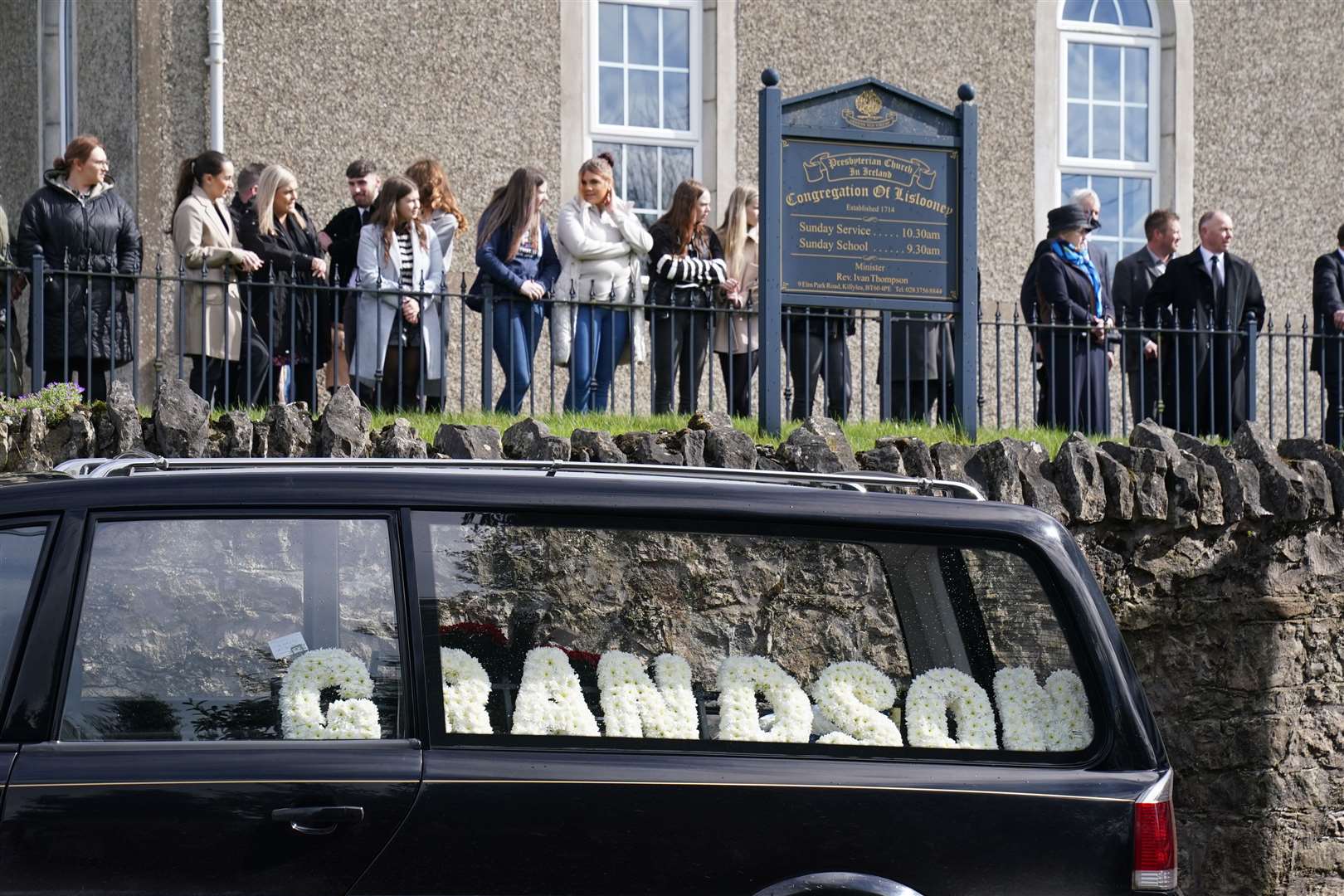 Mourners and a hearse with floral tributes outside Lislooney Presbyterian Church (Brian Lawless/PA)