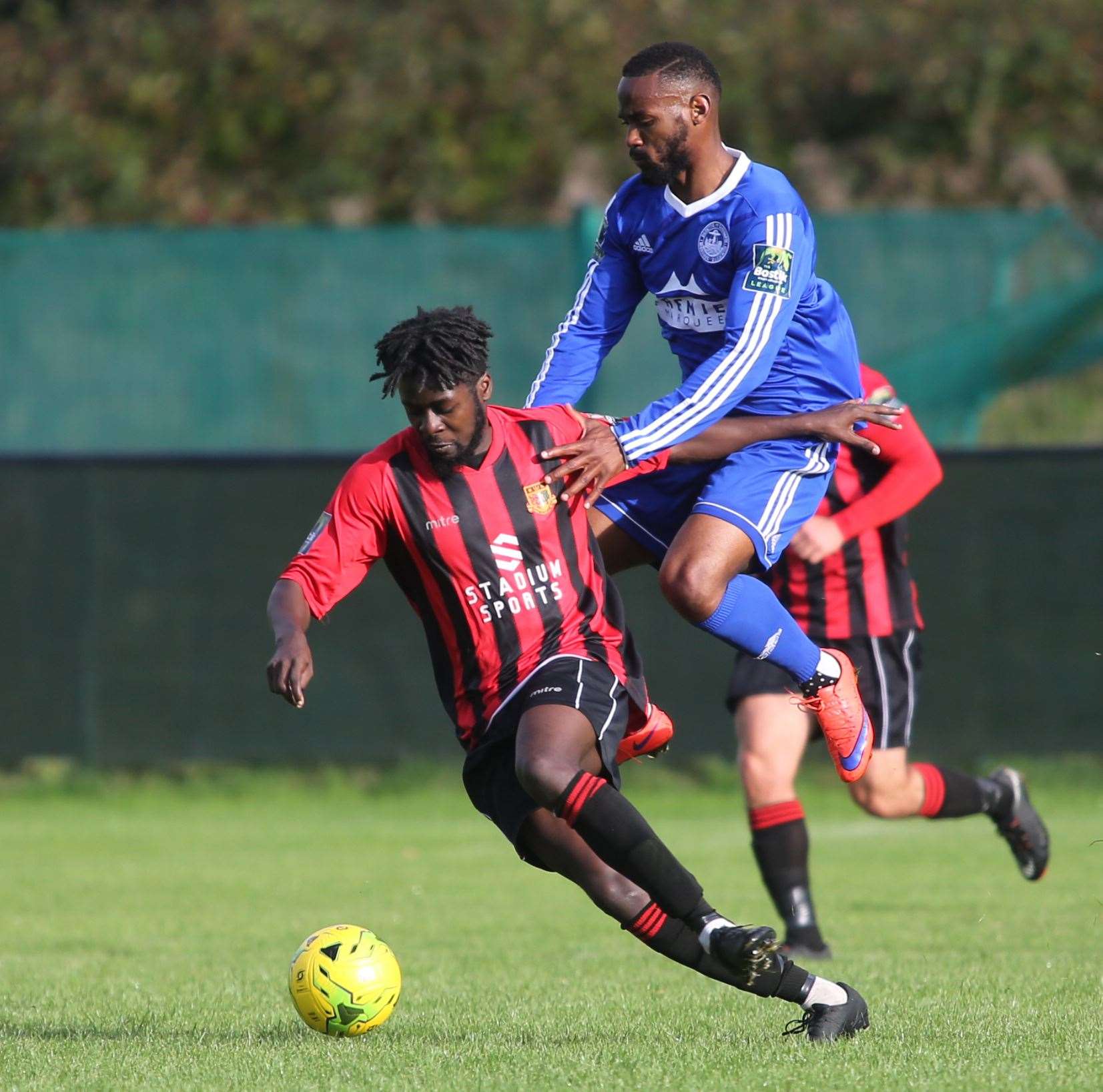 Jerson Dos Santos for Hythe in blue plays against for Bola Dawodu Sittingbourne in red and black at Sittingbourne Football Club. Picture by: John Westhrop FM4942636 (13881036)