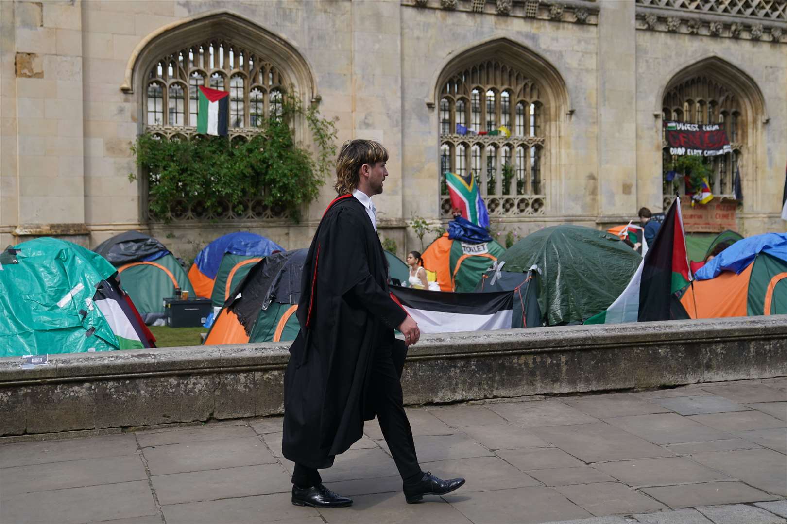 A graduating student walks past the Gaza protest encampment at Cambridge University (Joe Giddens/ PA)