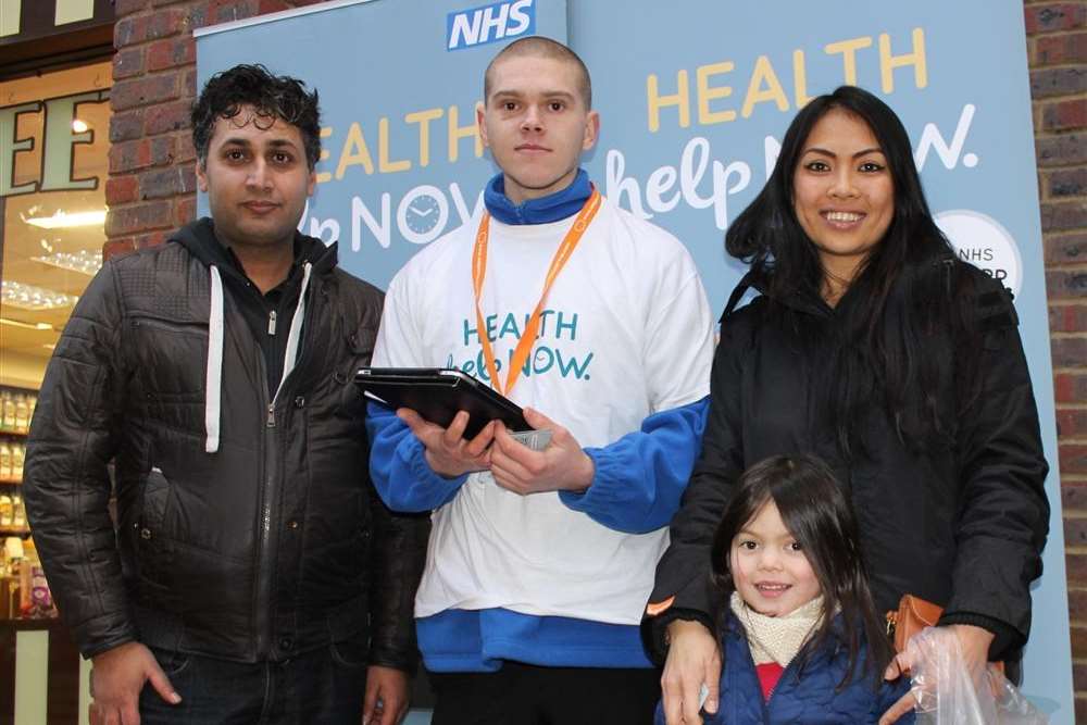 The NHS Health Help Now app is demonstrated by Joe Linnell (centre) to Ghazi Jan (left) and Priya Ponton with her four-year-old daughter, Georgia