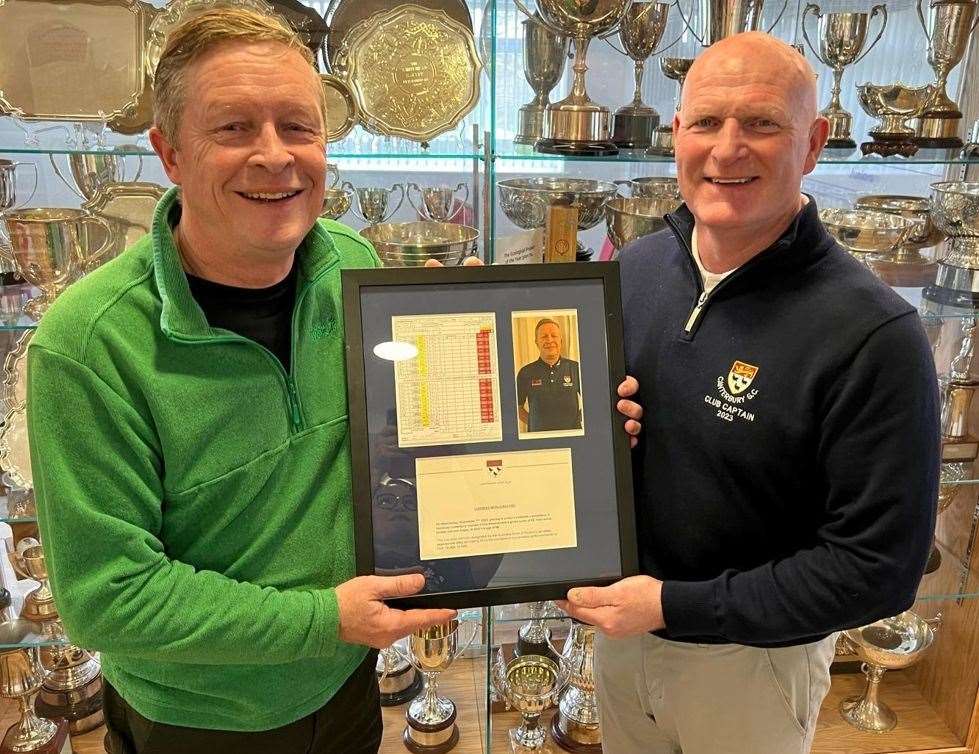 Chris Almond, left, receives a framed scorecard, picture and written declaration commemorating his record-busting gross 65 from 2023 captain Mark Broadhurst