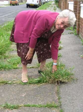 Trixie Hayes tries in vain to pull out stubborn weeds from the pavement outside her home